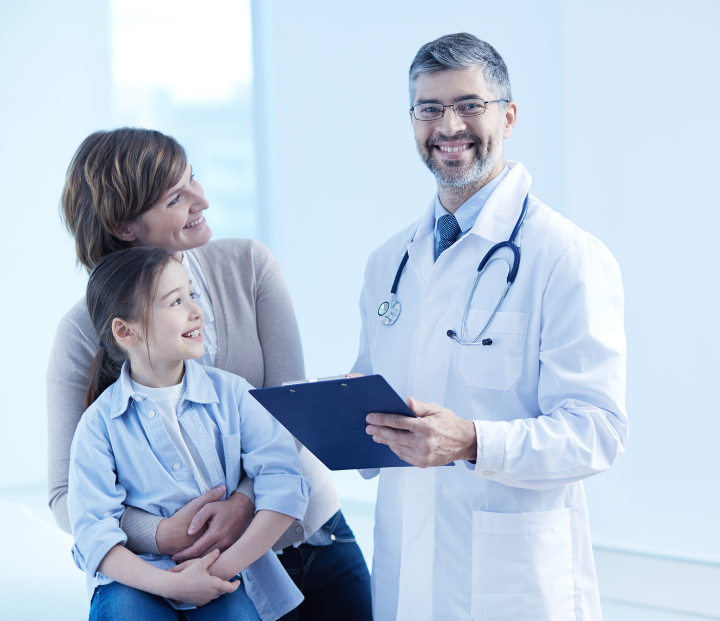 Imagem de um doutor cuidando de seus pacientes. Na cena está uma mulher segurando a sua filha e ambas sorrindo. Doutor segurando uma prancheta azul e sorrindo.