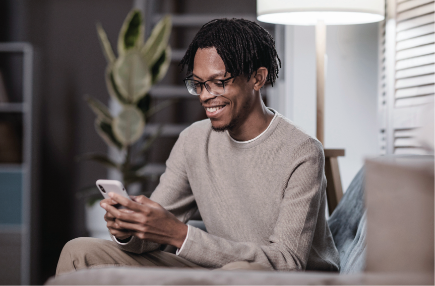 Homem moreno com óculos preto segurando um celular e sorrindo
